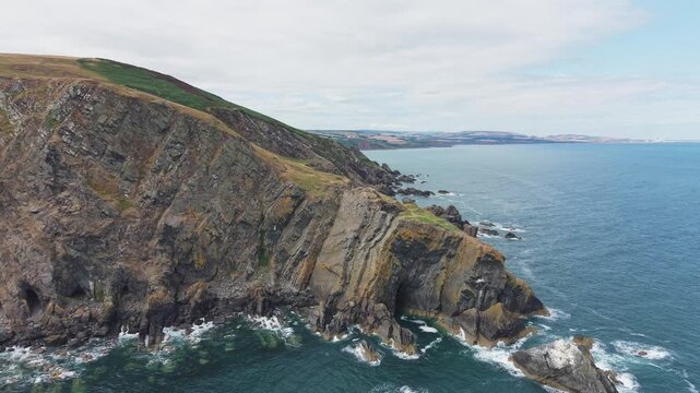 Aerial flight proceeding directly forward and flying over the massive, jagged sea cliff and dramatic rocky promontory at Fast Castle Head, Berwickshire, Scotland.