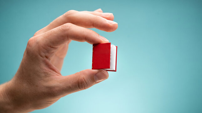 Hand holding a tiny red book symbolizing microlearning concept, bite-sized education, and quick knowledge sharing