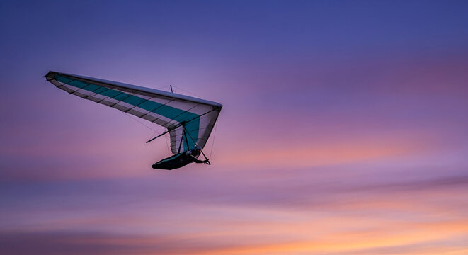 Hang glider soars against a vibrant purple and orange sky, representing freedom, adventure, and the thrill of flight