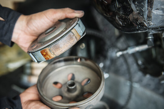 Mechanic inspecting glazed and worn scooter clutch shoes showing surface wear and friction loss