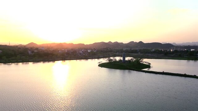 Aerial view of Buddhist pagoda on small island in peaceful lake at sunset in Ninh Binh, Vietnam. Scenic countryside with warm evening light and tranquil atmosphere.