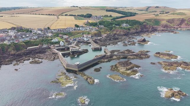 Aerial view of the fishing harbour, pier, and coastal village of St Abbs, highlighting the rocky shore and scenic countryside in Berwickshire, Scotland.