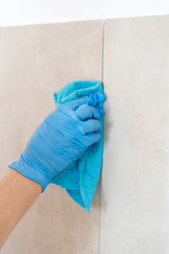 Close-up of person in blue nitrile glove wiping ceramic wall tiles with a microfiber cloth. Professional cleaning service or home maintenance concept.