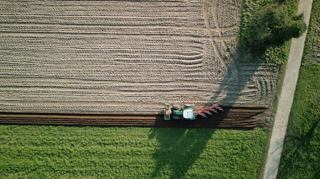 Green agriculture tractor with trailer ploughing field after winter, top view