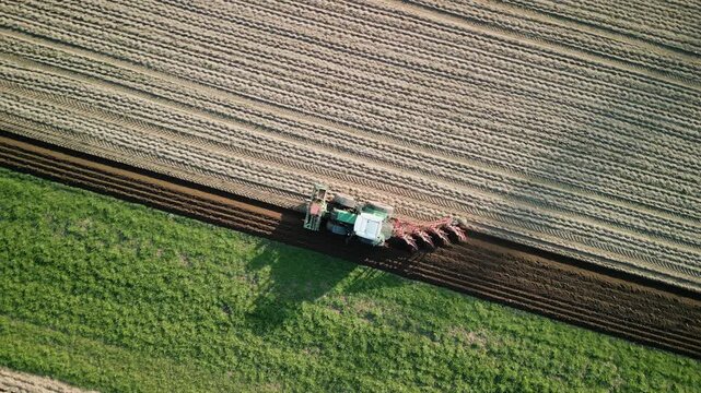 Tractor with trailer plowing field in spring, top drone view