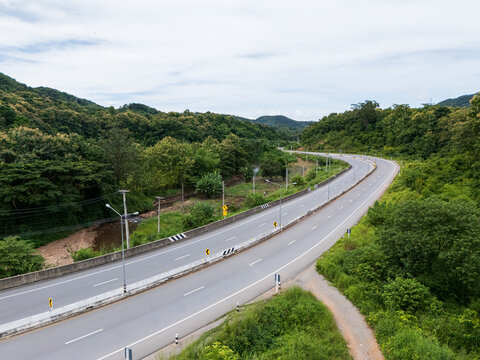 Aerial drone view of Highway 101 winding through lush green mountains between Phrae and Nan, Thailand. A scenic landscape of the road surrounded by tropical forest and a peaceful countryside