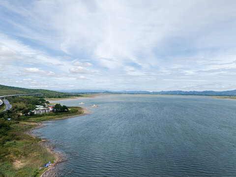 Drone aerial view of a large freshwater lake bordered by lush forest and distant mountains beneath expansive blue skies, showcasing natural landscape and tranquil scenery
