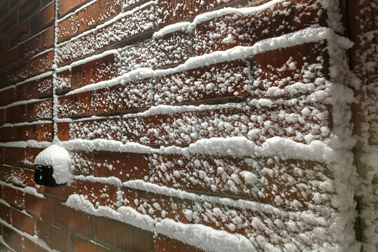 A brick wall covered in fresh snow after a winter snowfall. Snowflakes sticking to vertical surfaces during a blizzard with strong winds. Protecting buildings from cold and bad weather