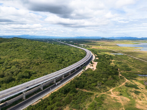 Drone aerial view of an elevated highway crossing lush forest and mountain landscape under dramatic clouds, The modern transportation infrastructure and nature concept