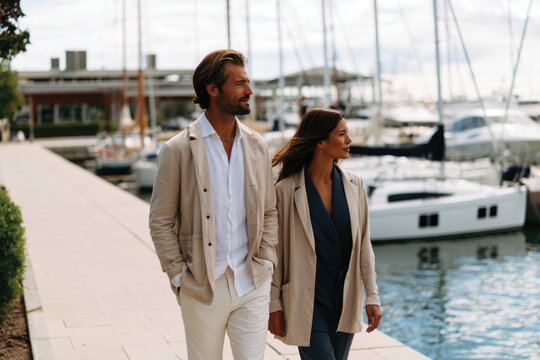 A charming couple dressed in contemporary attire enjoys a leisurely stroll by the waterfront, creating a perfect blend of style, romance, and lifestyle.