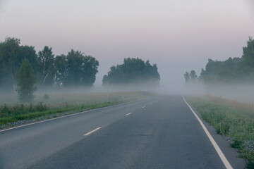 Obraz premium Car headlights glowing through thick morning fog on empty asphalt road