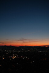 Fototapeta premium Fiery sunset horizon viewed from Mount Lycabettus in Athens, Greece, with the city below silhouetted beneath a glowing orange and blue twilight sky.