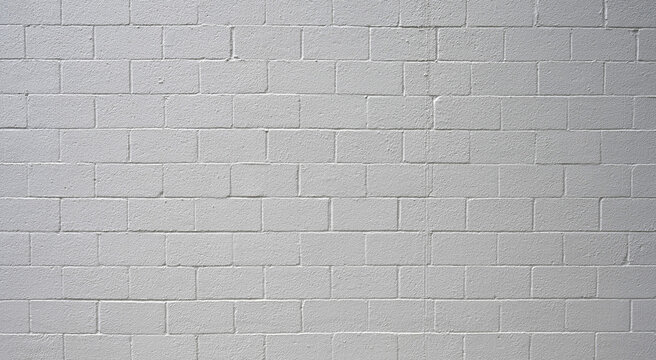 Horizontal view of painted white cinder block wall surface with flat CMU texture, porous, rough blocks, and rough painted mortar joints