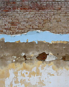 Vertical view of a run down multi layer wall surface with peeling paint in several colors revealing cracked concrete with holes exposing red brick and worn mortar underneath