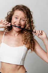 Naklejka premium Authentic beauty of a smiling middle aged woman with curly hair biting a strand, wearing a white crop top. Natural skin, unretouched, warm casual wellness mood.