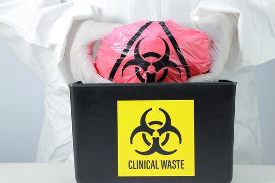 Cautious medical worker in white protective suit wearing glove performs hazard waste biohazard disposal inside clinical black bin