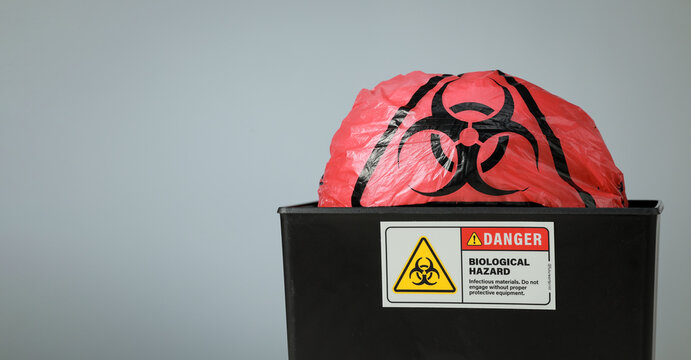 Red biohazard waste bag sits inside black disposal bin, evoking serious caution with clear medical danger warning sign on front