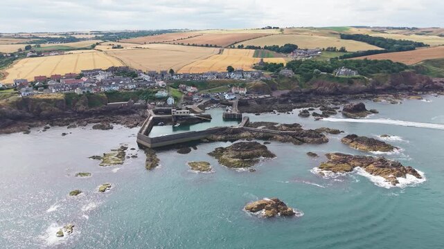 Aerial drone tracking shot over the historic fishing village and harbour of St Abbs, moving in a semi-circular motion to showcase the rugged Berwickshire coast, rocky bay, and North Sea in Scotland.