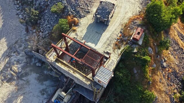 Workers are seen on a granite quarry site where heavy machinery is used to extract and process stones. The area shows piles of stone debris and equipment for mining activities.