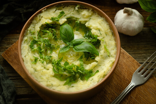 Bowl of mashed potatoes garnished with fresh herbs on rustic wooden table. Thanksgiving meal.