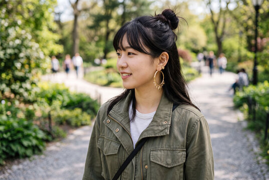 Young korean woman walking in a park wearing a casual jacket and backpack for lifestyle portrait and urban outdoor background