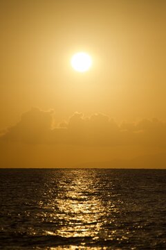 Sunlit ocean stretches beneath a warm golden sky with clouds along the horizon.