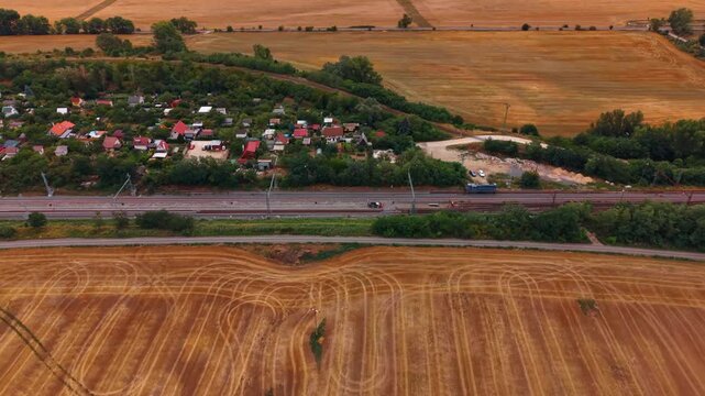 Railway maintenance beside allotment gardens and fields. Workers and equipment occupy parallel tracks between small garden houses and freshly harvested farmland.