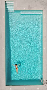 Top down view of a woman in redre swimsuit lying on her back in the pool.