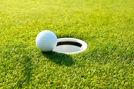 Golf ball on edge of cup close-up on bright green grass golf course putting hole detail sunny bright day sport