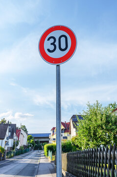 Speed limit 30 sign on a residential street with houses and trees