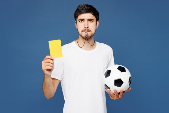 Young sad man fan wear white t-shirt cheer up support football sport team hold soccer ball yellow card propose player retire from field whistle, watch tv live stream isolated on plain blue background