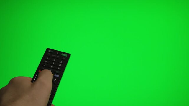 Hand holding remote control pointing at green screen TV mockup.