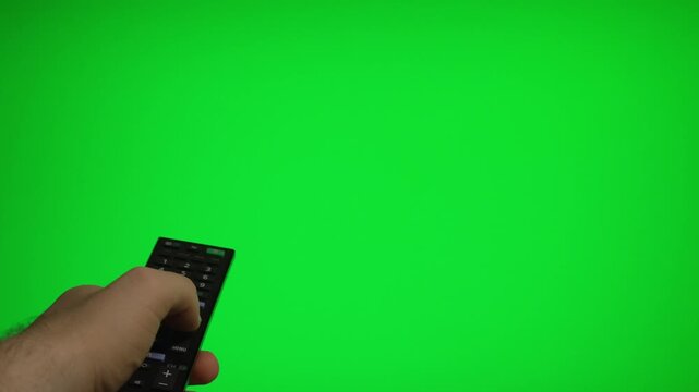 Hand holding remote control pointing at green screen TV mockup.