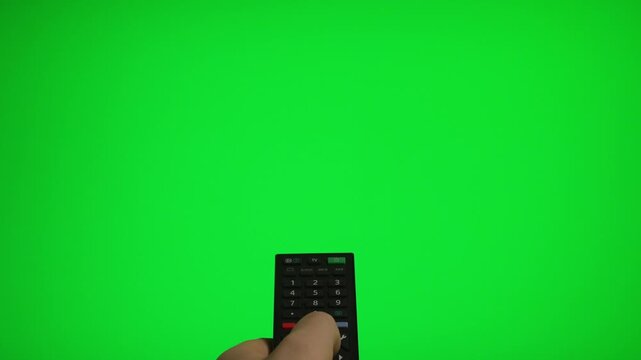 Hand holding remote control pointing at green screen TV mockup.