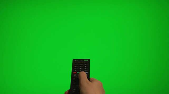Hand holding remote control pointing at green screen TV mockup.
