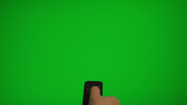 Hand holding remote control pointing at green screen TV mockup.