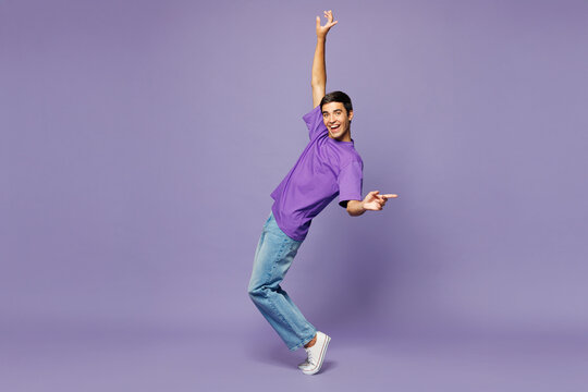 Full body young man wear violet t-shirt casual clothes standing on toes dancing lean back have fun spreading hands isolated on plain pastel light purple background studio portrait. Lifestyle concept.