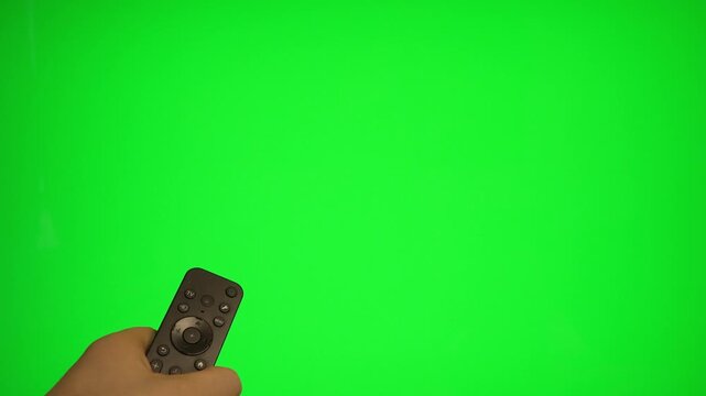 Hand holding remote control pointing at green screen TV mockup.