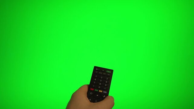 Hand holding remote control pointing at green screen TV mockup.