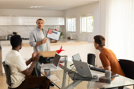 Diverse male team presenting framed certificate in modern kitchen with laptops and gift box