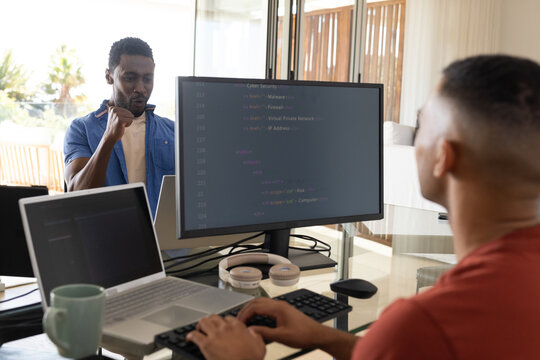 African American male coworkers coding at glass desk with code on monitor, copy space