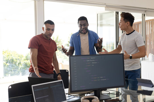 Diverse male coworkers discussing code on large monitor at modern office with laptops