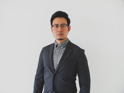 Serious Asian businessman in dark suit and glasses, professionally looking at camera.