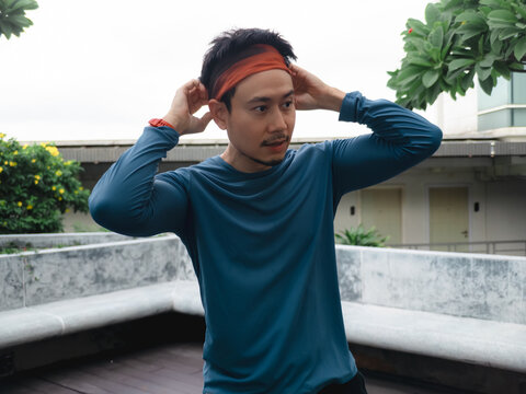 Active Asian man in athletic wear adjusting his headband, ready for outdoor fitness.