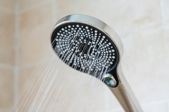 A close-up view of a handheld showerhead spraying a steady stream of water, designed for bathroom use.