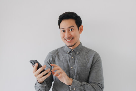 Happy young Asian man using a smartphone, looking at the camera with a surprised smile.