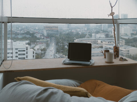 Cozy indoor workspace with laptop overlooking a rainy city view from a high-rise window
