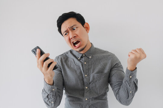 Angry Asian man shouting at his smartphone, expressing intense frustration and disappointment.