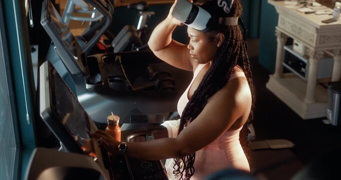 Smiling Black woman selects a virtual route, puts on a VR headset and starts running on a treadmill in a smart gym, enjoying an immersive workout and exploring a virtual world.