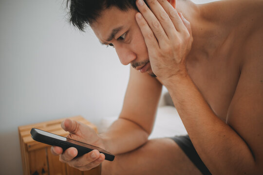 Young Asian man looking at smartphone with worried expression, feeling stressed and anxious